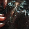 Person applying treatment to low porosity hair, showcasing the intricate texture and shine during a hair care routine