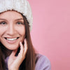 Smiling woman in a white beanie and purple sweater, showing glow of face.