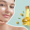 Close-up of a woman with glowing skin next to a bottle of olive oil and scattered olives, symbolizing the use of natural oils in skincare